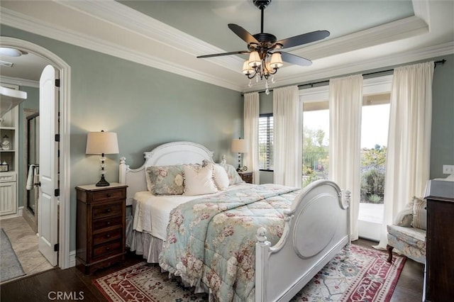 bedroom featuring a tray ceiling, wood finished floors, access to exterior, arched walkways, and crown molding