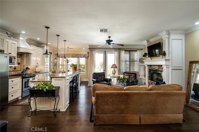 living room with ornamental molding, a fireplace, ceiling fan, and dark wood-type flooring