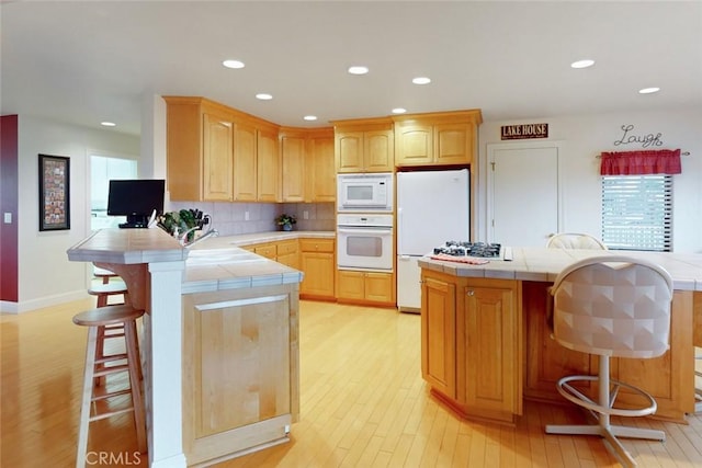 kitchen with tile countertops, a breakfast bar, kitchen peninsula, decorative backsplash, and white appliances