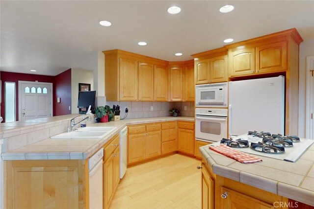 kitchen with kitchen peninsula, sink, white appliances, light hardwood / wood-style flooring, and tile counters