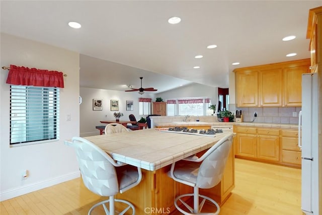 kitchen with a kitchen bar, tile counters, decorative backsplash, white appliances, and vaulted ceiling