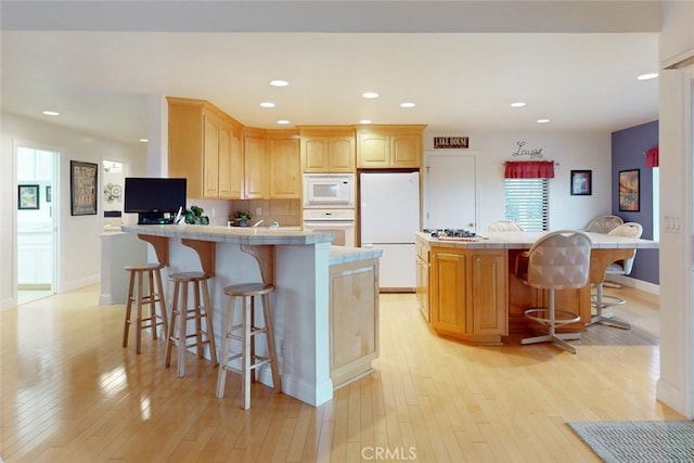 kitchen featuring light brown cabinets, white appliances, a breakfast bar area, and a kitchen island