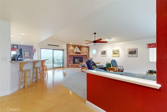 living room with ceiling fan, vaulted ceiling, a fireplace, and light hardwood / wood-style flooring