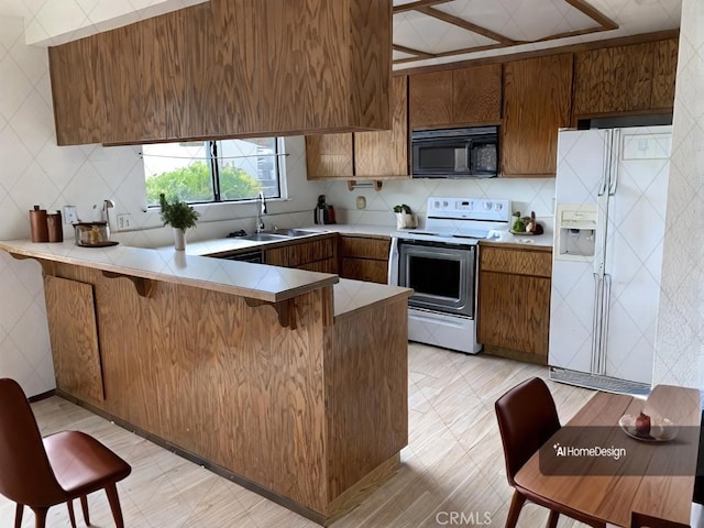 kitchen with white appliances, brown cabinetry, a peninsula, light countertops, and a sink