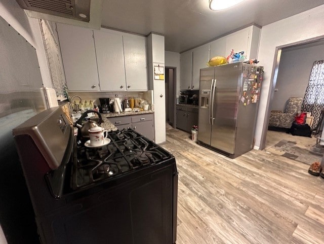 kitchen with white cabinetry, stainless steel fridge, black gas range oven, and light wood-type flooring