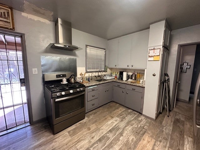 kitchen featuring gray cabinetry, stainless steel range with gas cooktop, wood-type flooring, and wall chimney range hood