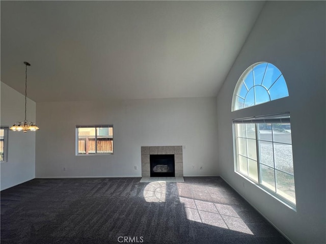 unfurnished living room with a tiled fireplace, high vaulted ceiling, dark carpet, and a notable chandelier