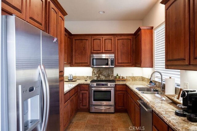 kitchen featuring light stone counters, appliances with stainless steel finishes, sink, and backsplash