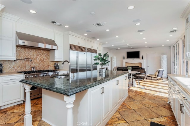 kitchen featuring sink, wall chimney exhaust hood, high end appliances, and white cabinetry