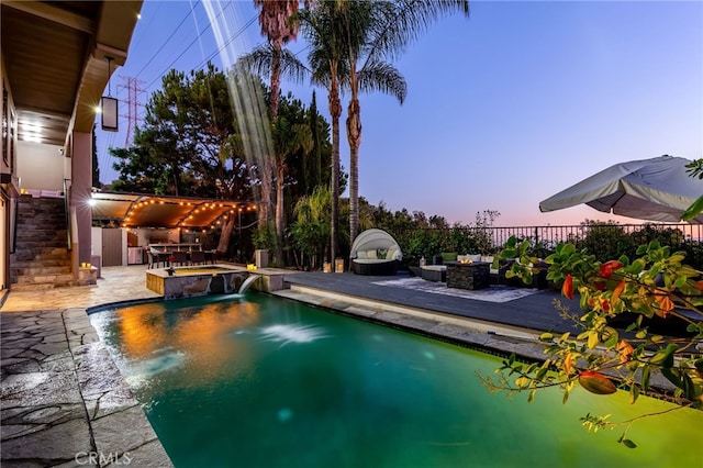 pool at dusk featuring a patio area, pool water feature, an in ground hot tub, and exterior kitchen