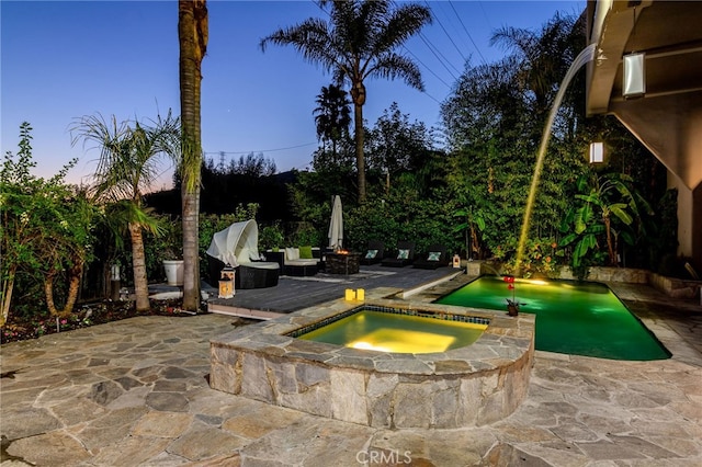 pool at dusk featuring an in ground hot tub and a patio area