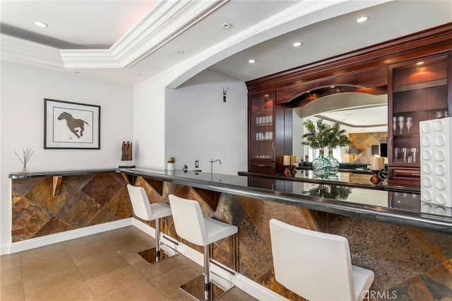 bar featuring dark stone counters, crown molding, and tile patterned floors