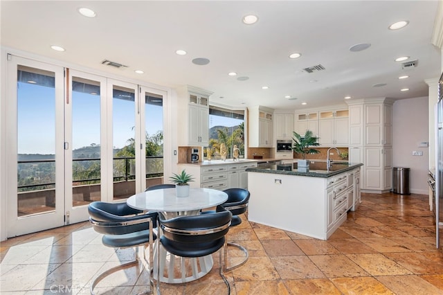 kitchen with decorative backsplash, dark stone countertops, white cabinetry, and a center island with sink