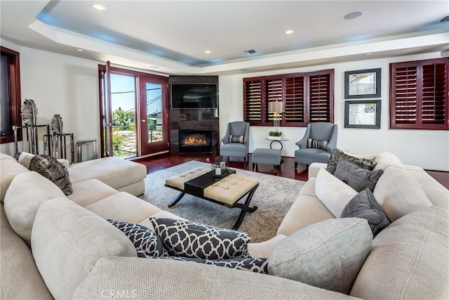 living room featuring french doors, hardwood / wood-style flooring, a tray ceiling, and a tiled fireplace