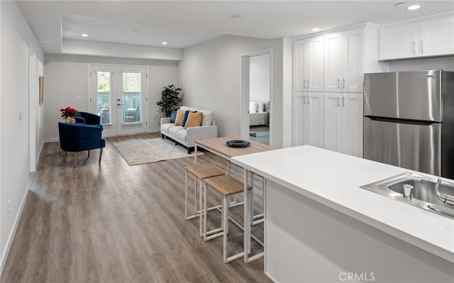 kitchen with french doors, a kitchen bar, white cabinetry, light hardwood / wood-style floors, and stainless steel refrigerator