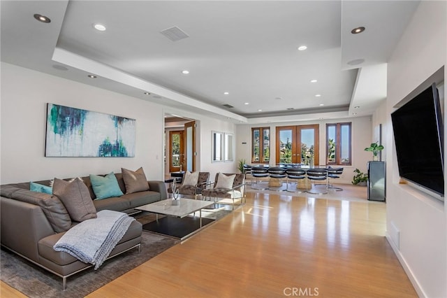 living room with french doors, light wood-type flooring, and a raised ceiling