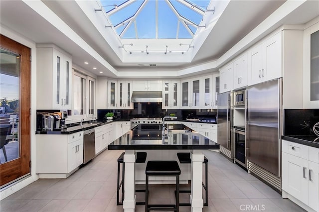 kitchen with a kitchen breakfast bar, a raised ceiling, sink, built in appliances, and a center island with sink