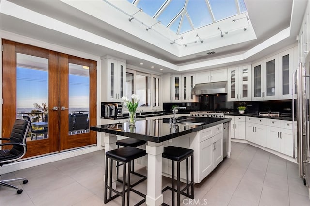 kitchen with french doors, sink, white cabinets, a breakfast bar area, and an island with sink