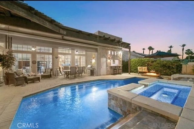 pool at dusk with an in ground hot tub and a patio