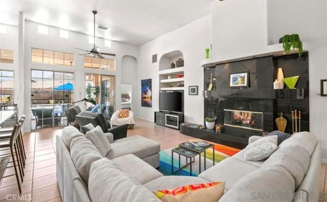 living room featuring ceiling fan, a fireplace, built in features, and light tile patterned floors