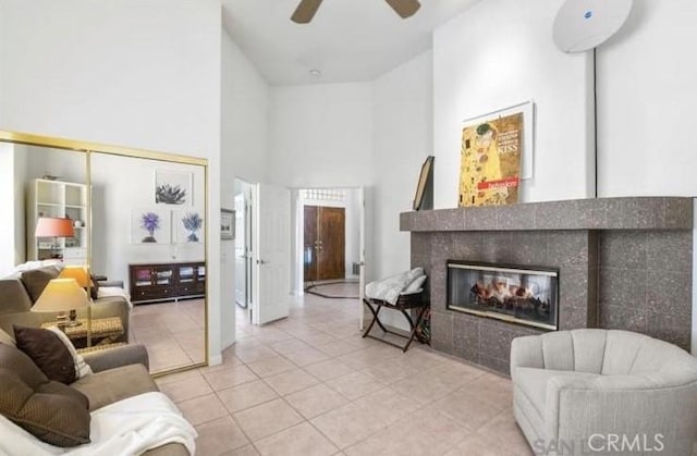 living room with light tile patterned floors, a tile fireplace, ceiling fan, and a high ceiling