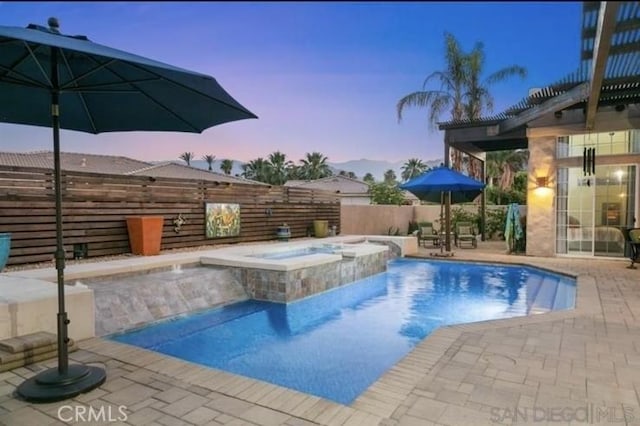 pool at dusk with an in ground hot tub and a patio