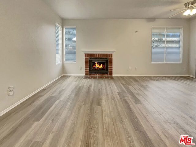 unfurnished living room featuring a brick fireplace, light wood-type flooring, and ceiling fan