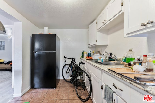 kitchen featuring black fridge, sink, light tile patterned floors, a textured ceiling, and white cabinetry