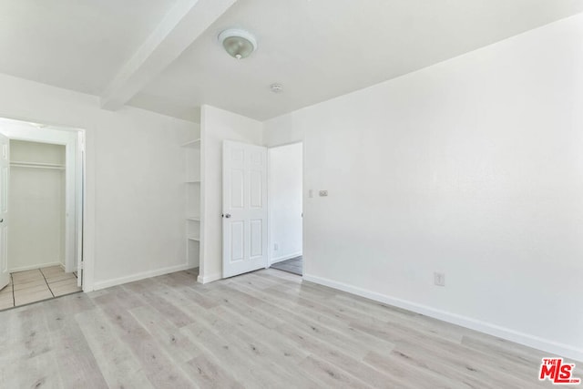 unfurnished bedroom with light hardwood / wood-style floors, beamed ceiling, and a closet