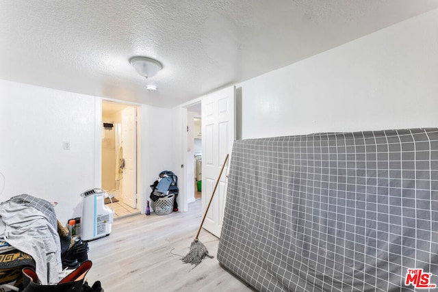 bedroom with light wood-type flooring, tile walls, and a textured ceiling