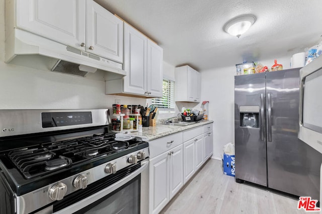 kitchen featuring light stone counters, white cabinets, stainless steel appliances, light wood-type flooring, and a textured ceiling