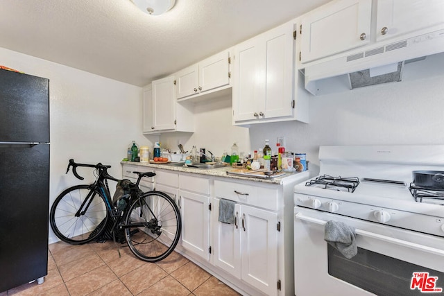 kitchen with white cabinetry, white gas range oven, light tile patterned floors, sink, and black fridge