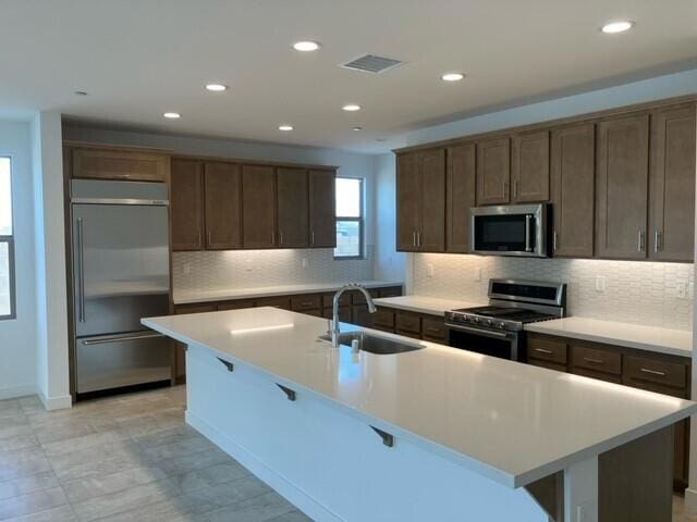 kitchen featuring an island with sink, stainless steel appliances, backsplash, and sink