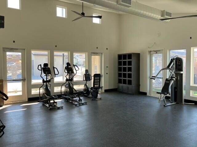 gym featuring a towering ceiling, ceiling fan, and a wealth of natural light