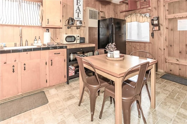 kitchen featuring tile countertops, wooden walls, sink, black fridge, and light brown cabinets