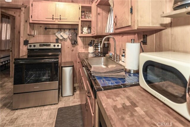 kitchen with stainless steel range with electric stovetop, butcher block counters, sink, and wooden walls