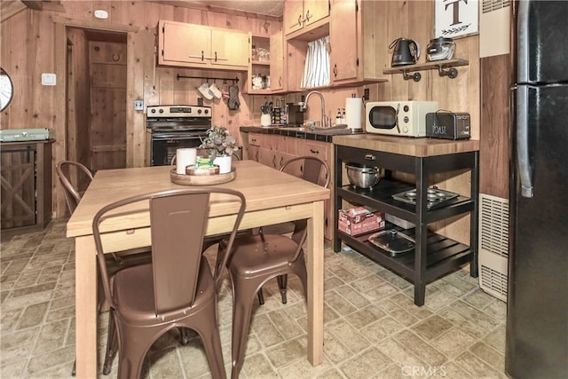 kitchen featuring black refrigerator, stove, sink, and wooden walls