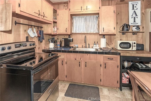 kitchen featuring sink, stainless steel electric range oven, light brown cabinets, wooden walls, and tile counters