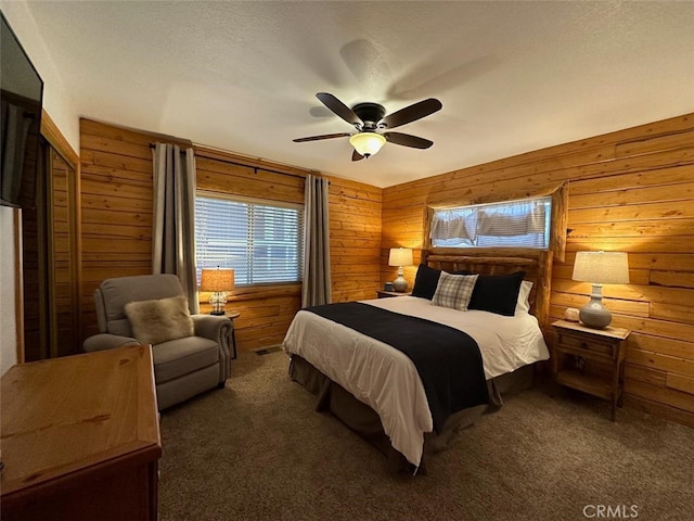 bedroom with a textured ceiling, wood walls, dark colored carpet, and ceiling fan