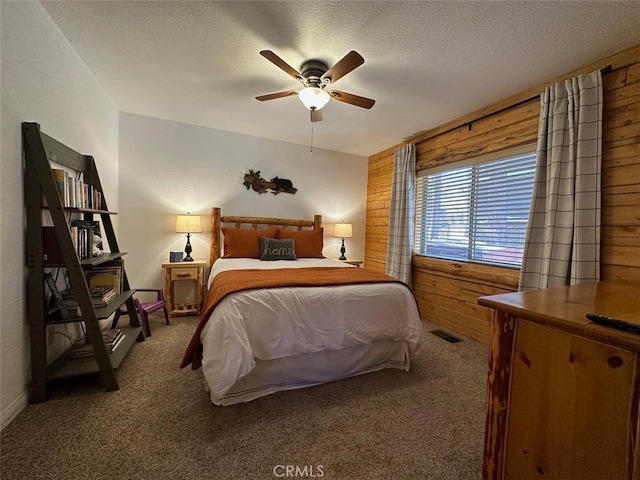 bedroom with a textured ceiling, carpet, wooden walls, and ceiling fan