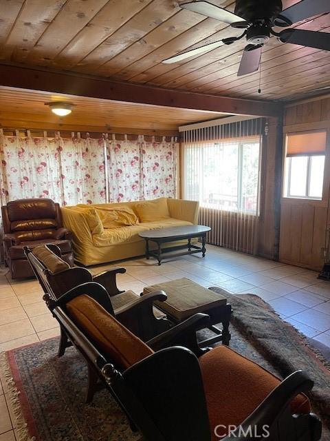 tiled living room featuring beamed ceiling, wood walls, ceiling fan, and wood ceiling