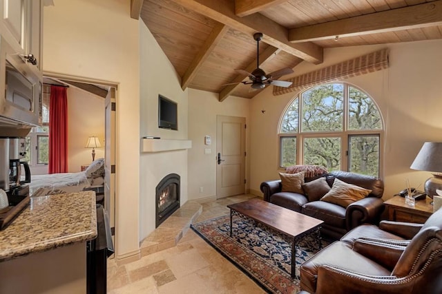 living room with vaulted ceiling with beams, wood ceiling, ceiling fan, and a fireplace