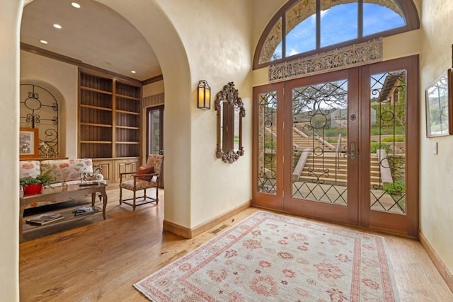 foyer featuring wood-type flooring, ornamental molding, french doors, and a high ceiling