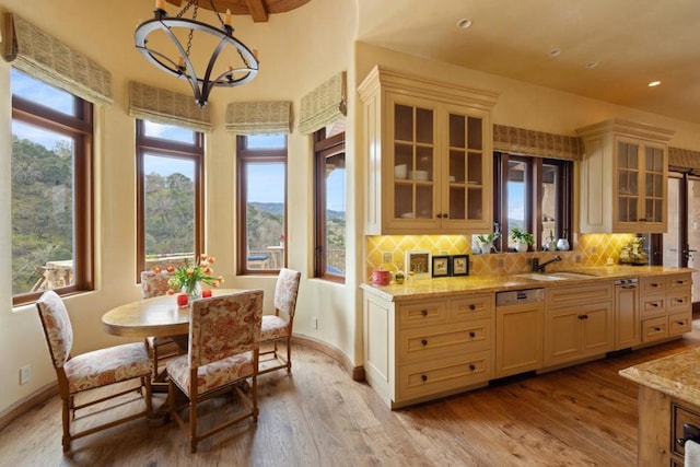 kitchen featuring pendant lighting, dishwashing machine, decorative backsplash, light hardwood / wood-style floors, and light stone countertops