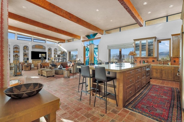 kitchen with beamed ceiling, a kitchen breakfast bar, light stone counters, and a wealth of natural light