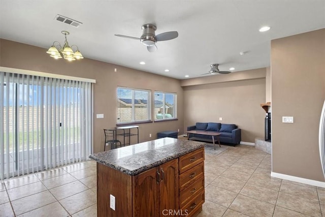 kitchen with hanging light fixtures, ceiling fan with notable chandelier, light tile patterned floors, and dark stone counters