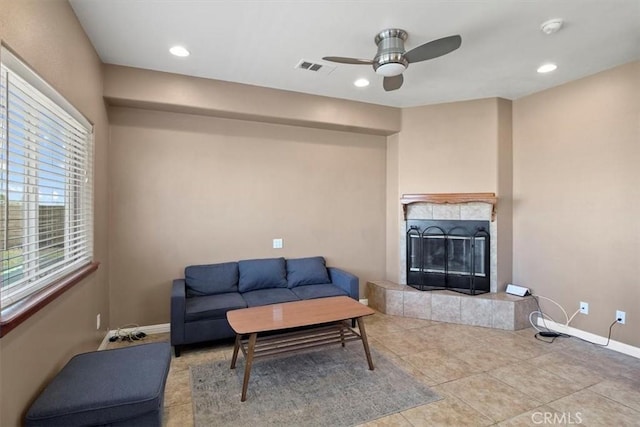 living room with ceiling fan, a tiled fireplace, and light tile patterned floors