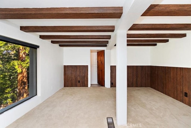 unfurnished room with beam ceiling, light colored carpet, and wooden walls