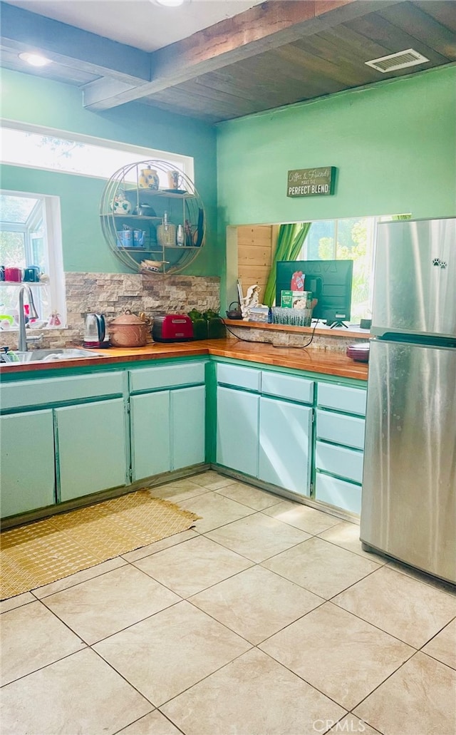 kitchen featuring beamed ceiling, stainless steel fridge, light tile patterned floors, and sink