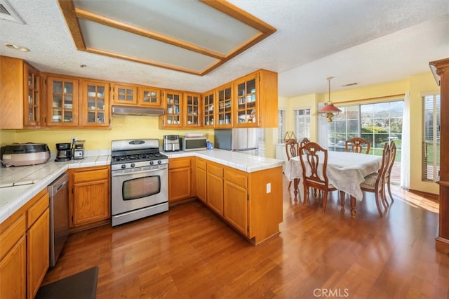 kitchen featuring hanging light fixtures, kitchen peninsula, wood-type flooring, a textured ceiling, and stainless steel appliances